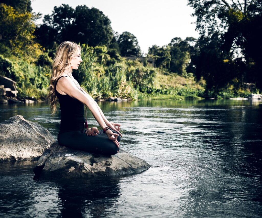 Francesca d’Errico in meditazione, seduta in padmasana su una roccia in mezzo a un fiume