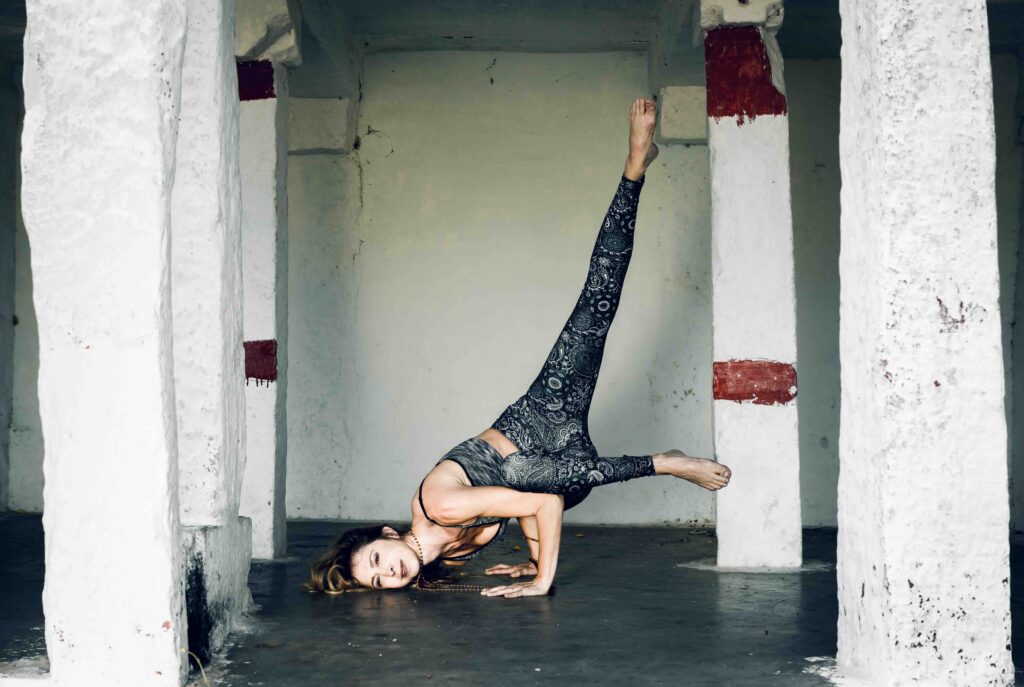 Francesca d’Errico in una posizione di Ashtanga Yoga con una gamba sollevata, tra le colonne di un portico
